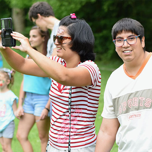 young adults enjoying a family event, one has face-paint and is taking a picture with their phone