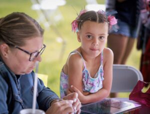 Child looking at camera with staff helping her color